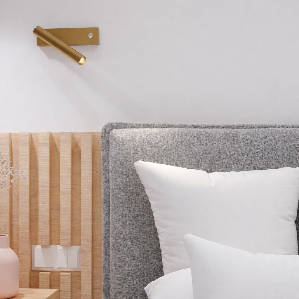 A gold LED wall sconce with an integrated switch by the bed.